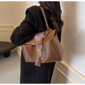 Detailed view of brown leather tote bag featuring a golden twist lock and shoulder strap