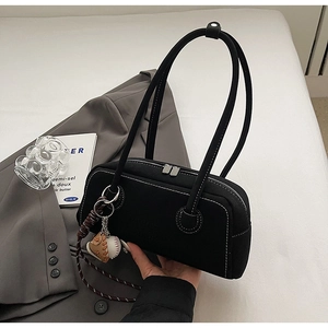 Detail view of black rectangular shoulder bag with white contrast stitching and baseball charm