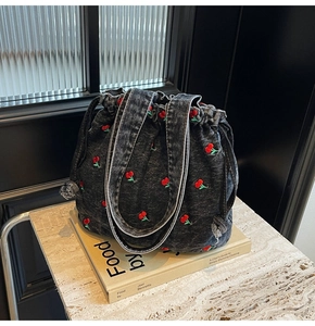 Detail of grey denim bucket bag with red cherry embroidery and drawstring closure
