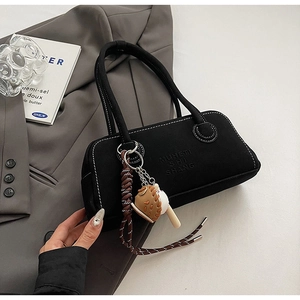 Detail of black baguette bag with white stitching and 3D bread-shaped pendant accessory