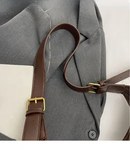Détail de la bandoulière réglable en cuir marron foncé avec boucle dorée sur un sac à main
