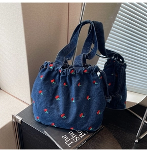 Close-up of dark blue denim bucket bag featuring vibrant red cherry embroidery details