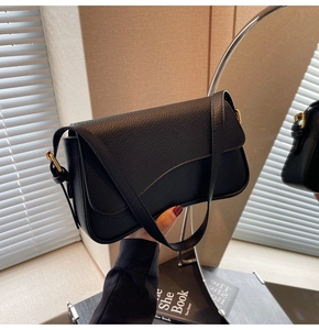 Detail of black lychee grain leather shoulder bag with gold hardware buckle and flap closure