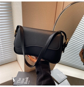 Detail of black lychee grain leather shoulder bag with golden buckle and adjustable strap