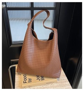 Détail d'un sac cabas en cuir tressé marron caramel posé sur une surface en marbre chic