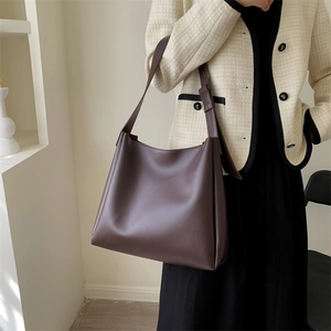 Deep brown tote bag worn over the shoulder with a neutral minimalist outfit and soft lighting