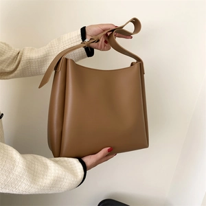 Minimalist tan leather tote bag shown being held to demonstrate size and draped structure