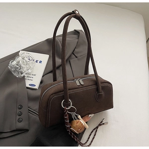 Close-up of brown suede shoulder bag with logo detail and baseball pendant on suit
