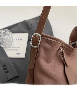 Close-up of brown suede shoulder bag featuring silver oval buckle and adjustable strap