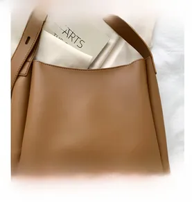 Detail of minimalist brown leather tote bag on white fabric background with prop book