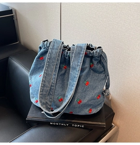 Detailed view of denim bucket bag with red cherry embroidery and drawstring closure