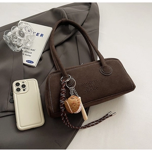 Detail of dark brown suede bag with unique baseball charm and embossed brand logo