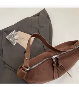 Détail d'un sac bandoulière en daim marron avec doubles fermetures éclair sur un blazer gris