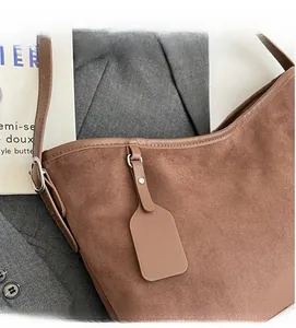 Detail of caramel suede crossbody bag with metal buckle and luggage tag accessory
