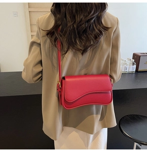 Detail of red leather shoulder bag with gold clasp and unique wavy flap design