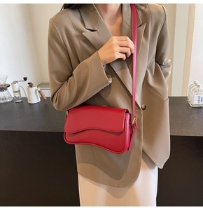 Close-up of red leather crossbody bag with wave-shaped flap and gold hardware detail