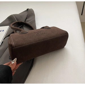 Detailed view of dark brown suede handbag featuring embossed lettering and white stitching