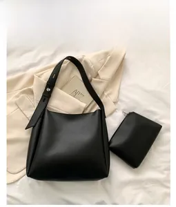 Flat lay of black tote bag and matching pouch on white fabric with beige blazer
