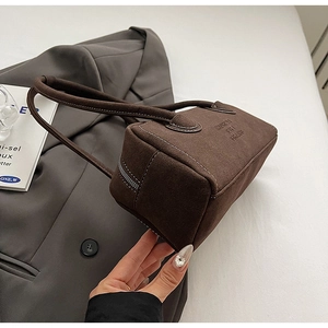 Detail of dark brown suede shoulder bag with embossed text on a grey blazer