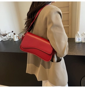 Detailed view of red pebble leather shoulder bag with wave flap design on a model