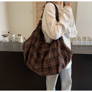 Gros plan d'un grand sac cabas à carreaux marron porté par un mannequin dans un café