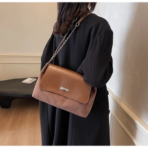 Detail shot of the retro brown suede shoulder bag featuring a silver logo and chain strap