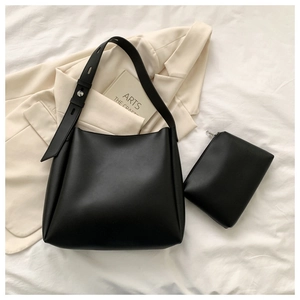 Detail of minimalist black matte leather hobo bag and matching zip pouch on white fabric