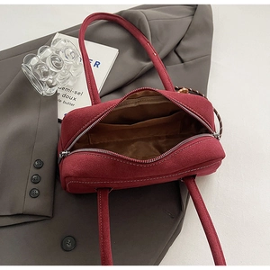 Detail view of burgundy suede shoulder bag with contrast stitching and brown fabric lining