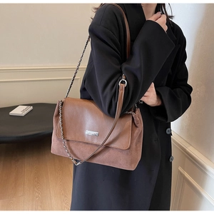 Detail view of brown patchwork underarm bag with silver logo plaque and chain strap