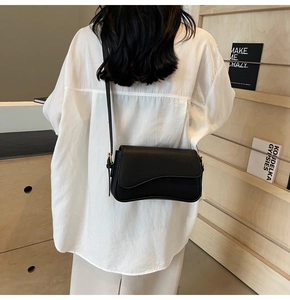 Detail of minimalist black pebbled leather crossbody bag with wave-cut flap and gold buckle