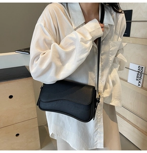 Detail shot of black lychee grain leather crossbody bag with curved flap on a female model