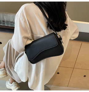 Side view of a black pebble leather shoulder bag worn by a model in a warm indoor setting