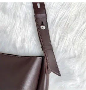 Detail of adjustable dark brown leather shoulder strap with silver metal buckle on bucket bag