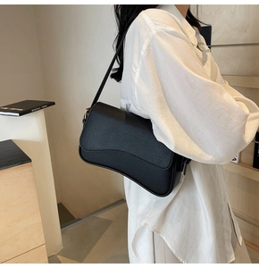 Detail of black litchi grain leather shoulder bag featuring a curved flap and gold hardware