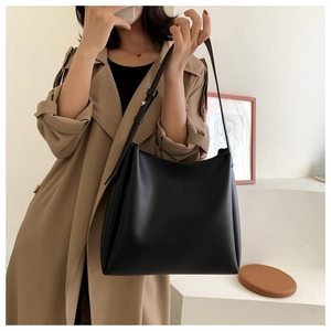 Close-up of a minimalist black matte leather tote bag worn with a chic beige trench coat
