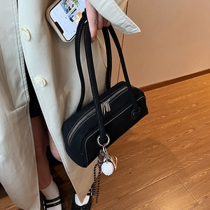 Minimalist black baguette shoulder bag with white contrast stitching and baseball charm