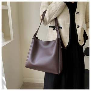 Dark brown leather tote bag worn by model with minimalist cream jacket and long skirt