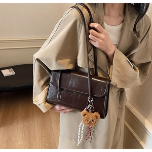 Détail du sac à bandoulière marron foncé brillant avec pendentif ours sur manteau beige