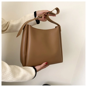 Close-up of brown synthetic leather tote bag with wide strap in minimalist interior