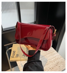 Detail of burgundy glossy faux leather shoulder bag with gold hardware and flap closure