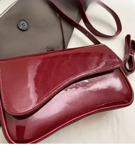 Detail of dark red patent leather handbag with curved flap and glossy mirror finish