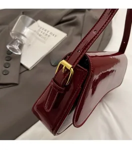 Detailed close-up of dark red patent leather bag showing gold buckle and glossy texture