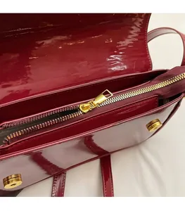 Close-up of glossy patent leather bag with gold metal zipper and magnetic buckle closure