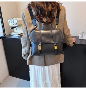Close-up of a retro dark gray leather backpack with metallic buckles in a cafe setting