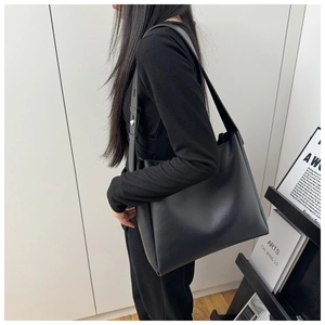 Detail view of black leather tote bag worn by model against minimalist white backdrop