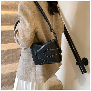 Detail of minimalist black leather shoulder bag showing contrast stitching and overlap structure