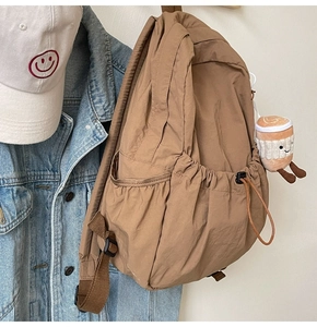 Detail of khaki nylon backpack featuring drawstring side pockets and plush coffee cup charm