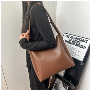 Detail of a large dark brown leather tote bag worn as a shoulder bag in a minimalist setting