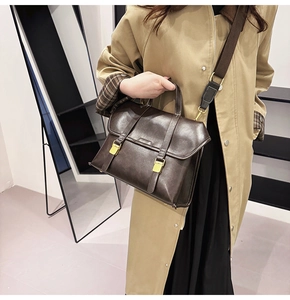 Detail of dark brown vintage satchel with gold buckles and wide fabric strap on model