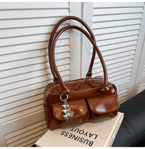 Detail of dark brown glossy leather handbag featuring dual pockets and silver heart charm